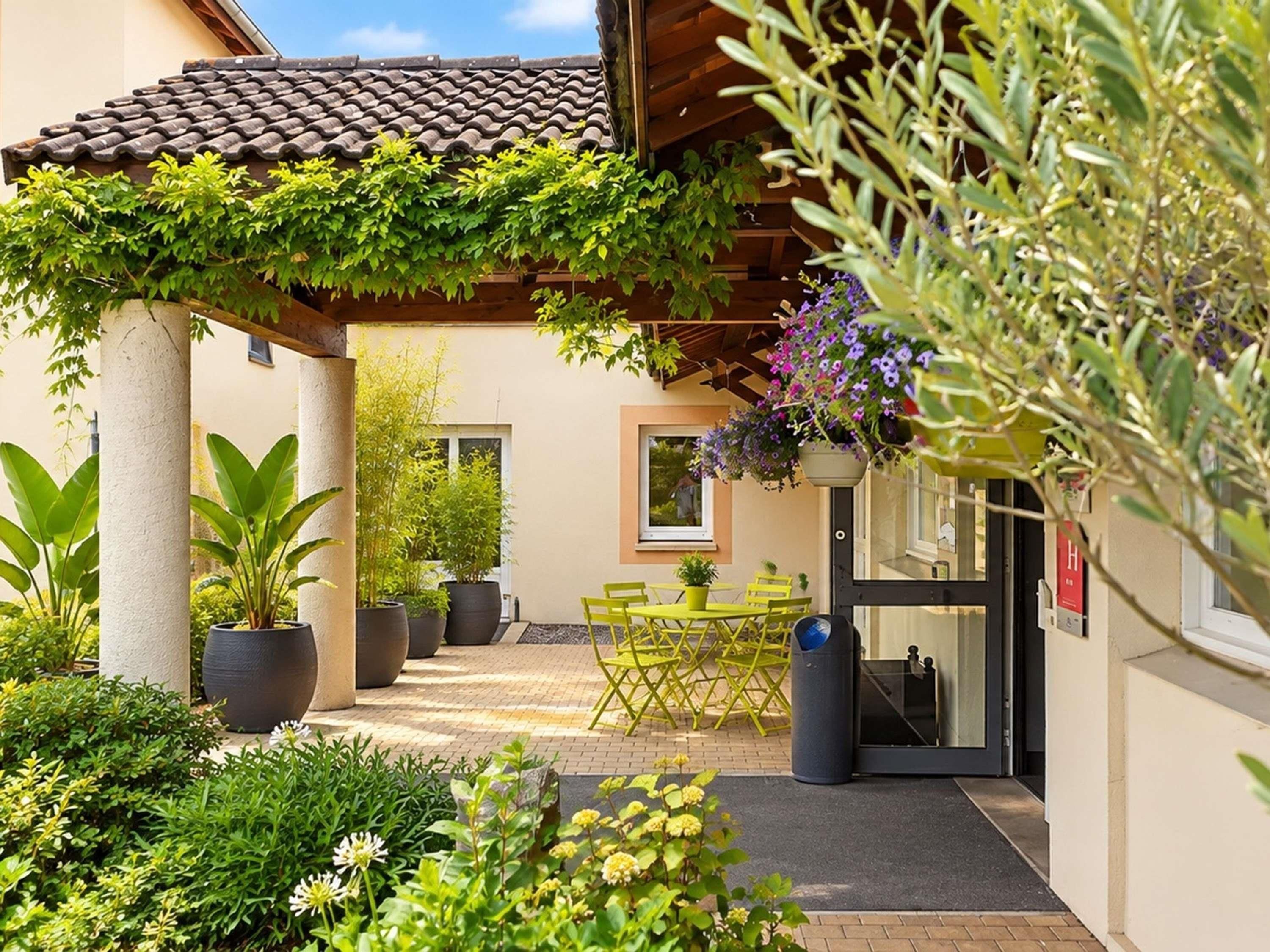A covered outdoor area with a table and chairs, potted plants, and a building entrance.