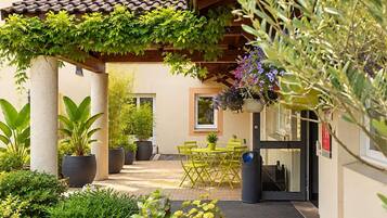 A covered outdoor area with a table and chairs, potted plants, and a building entrance.
