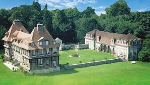 Een groot, historisch gebouw met meerdere vleugels, omgeven door een verzorgd gazon en bomen.