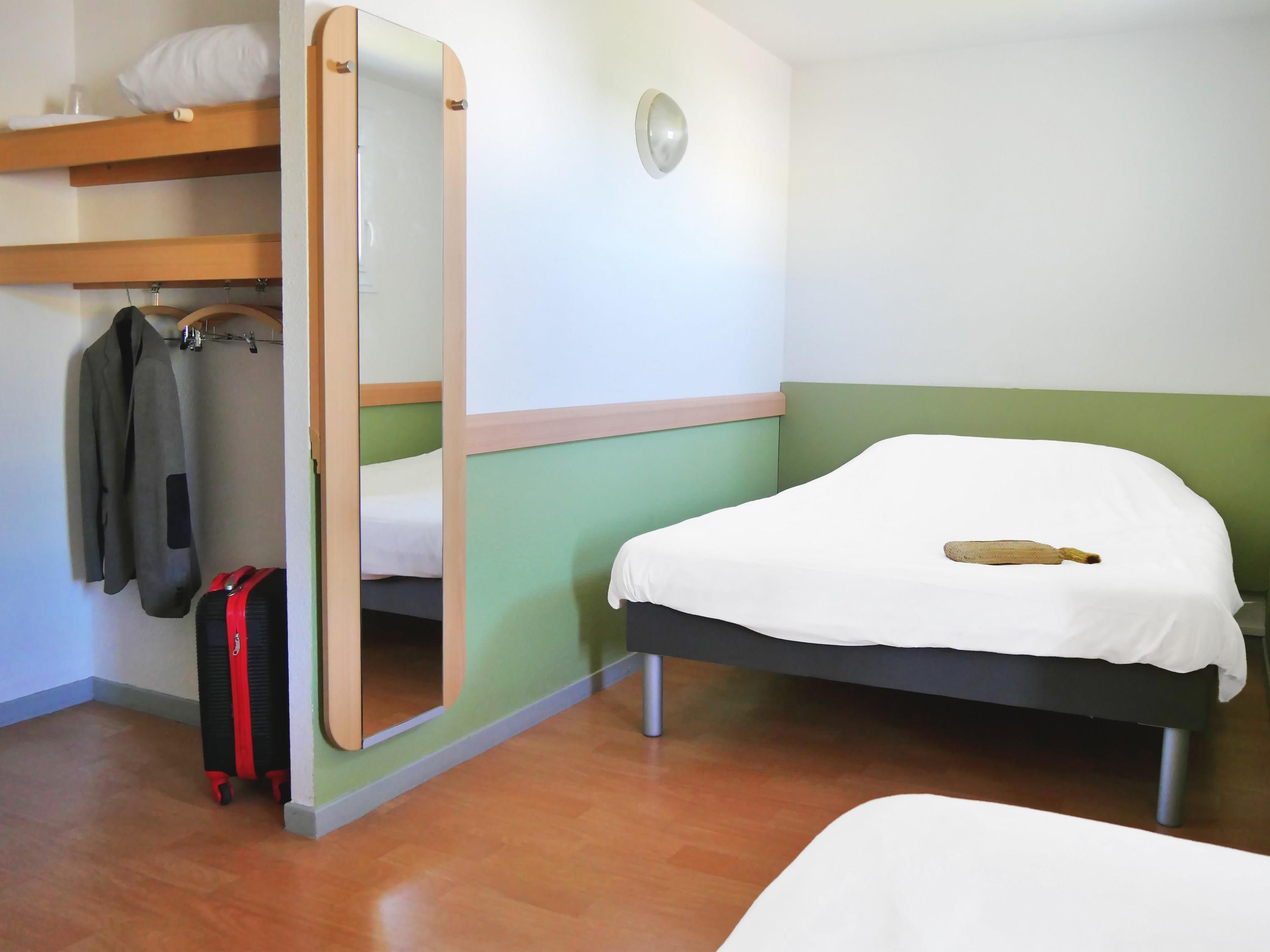 Ein Zimmer mit Bett, Koffer, Mantel und Spiegel.