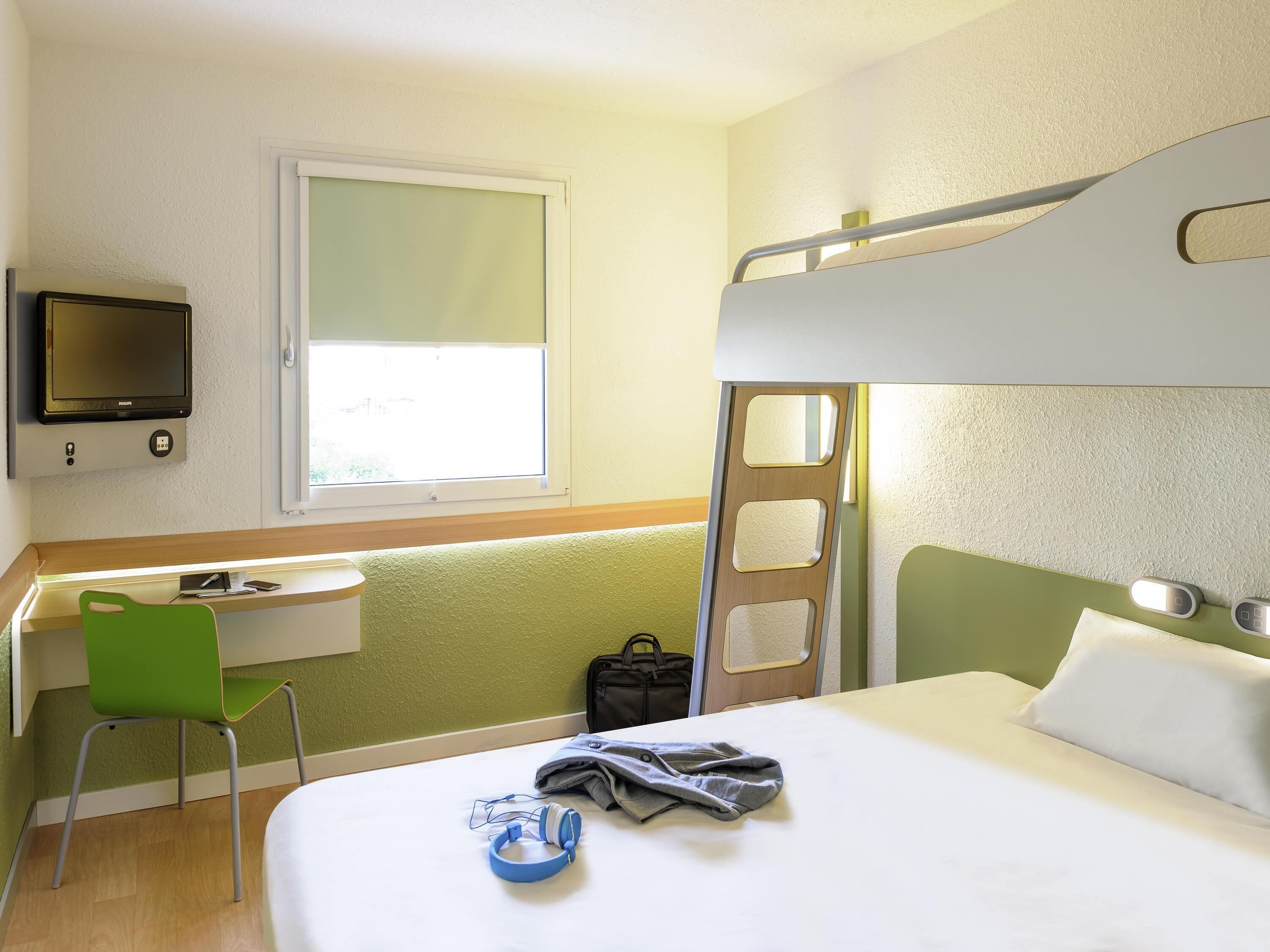 Een hotelkamer met een stapelbed, een bureau met stoel, een televisie en een raam.