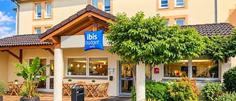 Un hotel con un letrero que dice 'ibis budget HOTEL' y un área de estar exterior cubierta con mesas y sillas.