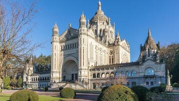 Un edificio histórico y majestuoso con múltiples torres y cúpulas, rodeado de jardines cuidados y senderos.