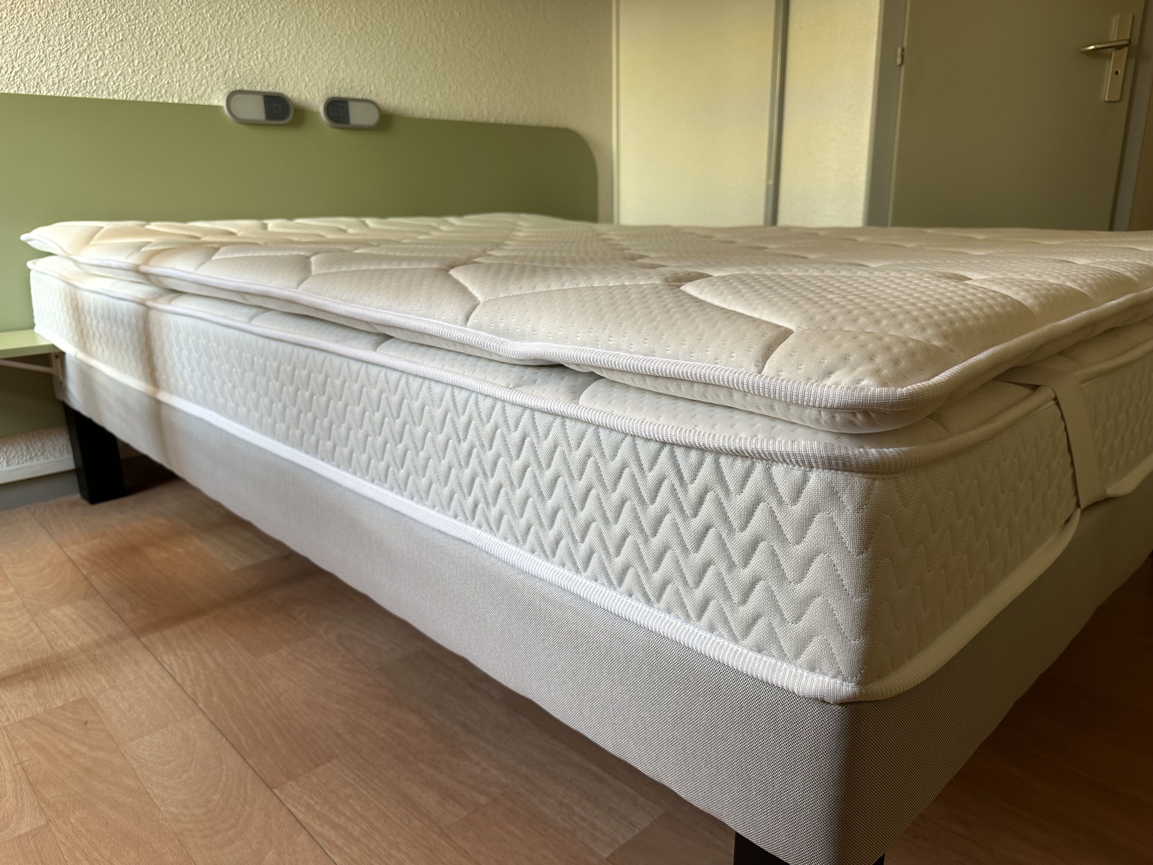 Un colchón en una habitación con cabecera verde y suelo de madera.