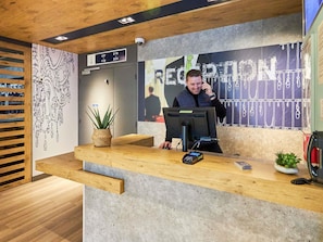 Una mesa de recepción con una computadora, una planta y un letrero con los números de las habitaciones.