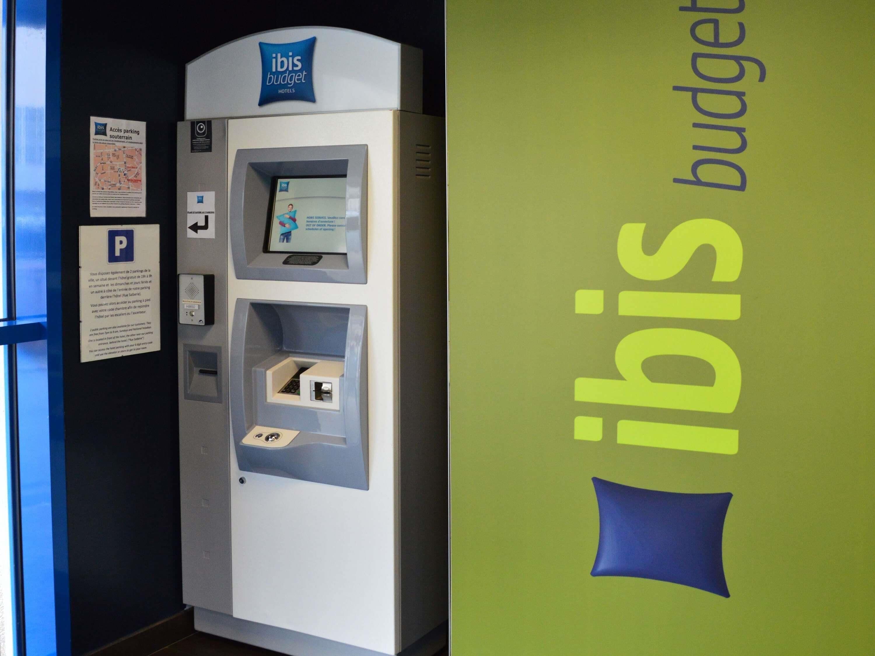 Quiosco de estacionamiento de ibis budget con pantalla digital, opciones de pago y señalización de estacionamiento.