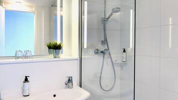 Een moderne badkamer met een douchecabine van glas, een wit wastafelmeubel met spiegel, en een plant in een pot op de vensterbank.