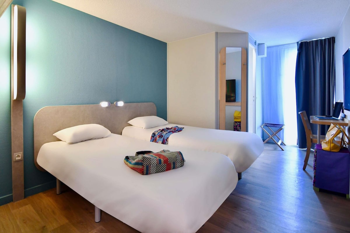 Une chambre d’hôtel avec deux lits, un bureau avec un ordinateur portable, une chaise et une petite table.