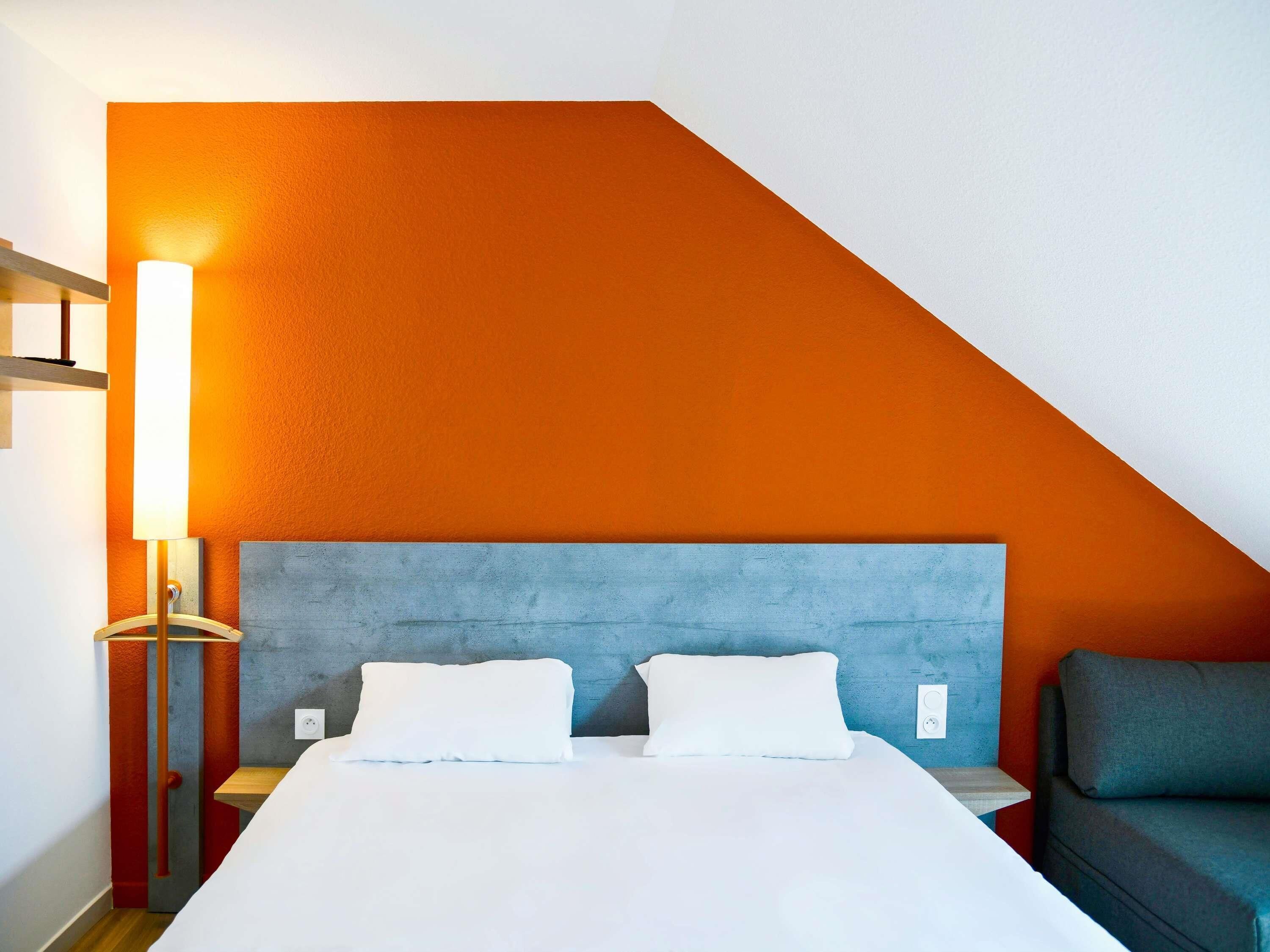 Hotellihuone, jossa on sänky, yöpöytä, lamppu, sohva ja seinä, jossa on geometrinen kuvio.