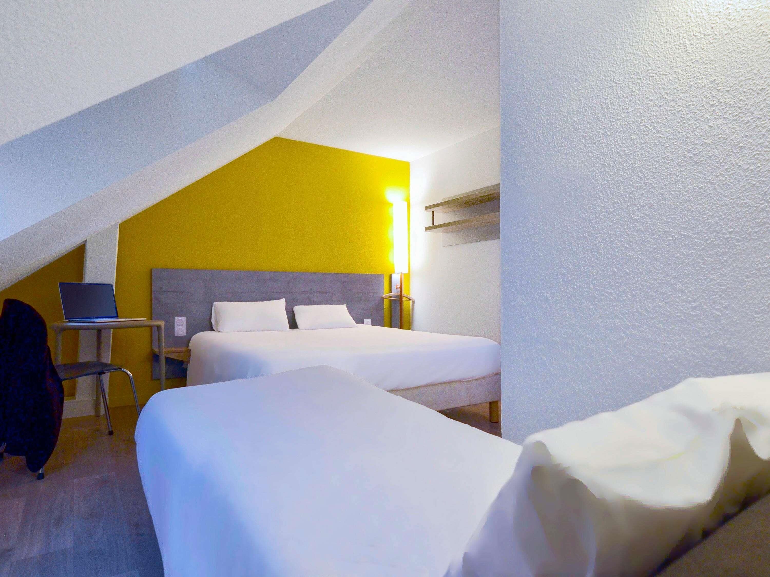 Een hotelkamer met twee bedden, een bureau met een laptop en een stoel.