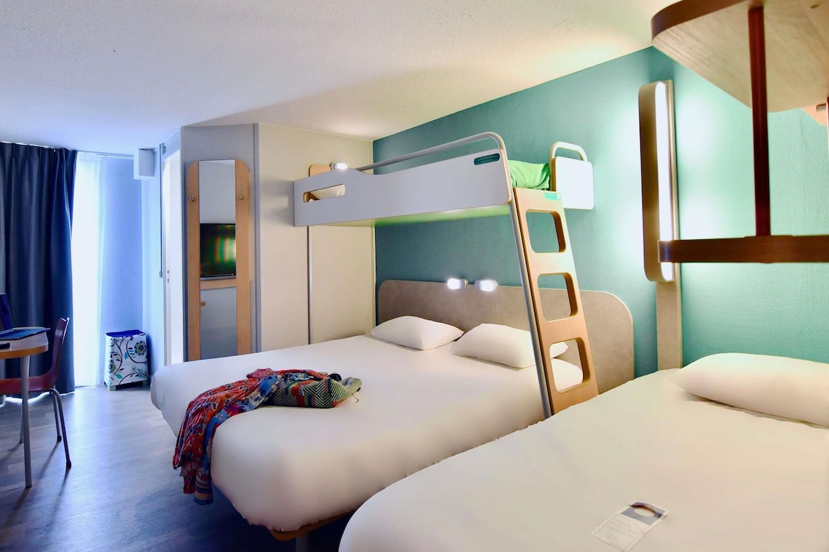 Une chambre d’hôtel avec des lits superposés, un bureau, une chaise, une télévision et une fenêtre avec des rideaux.