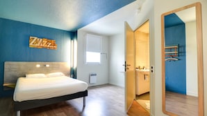 A modern bedroom with a bed, a mirror, a wardrobe, and a bathroom visible through an open door.