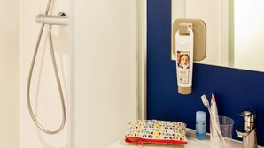 A bathroom with a shower, a mirror, a sink, and toiletries.