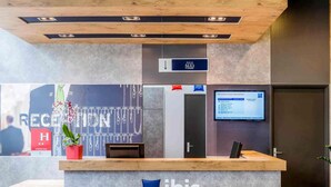 A reception desk with a sign for 'ibis budget Rueil-Malmaison,' a computer monitor displaying a webpage, and a wall with a large 'RECEPTION' sign. - ibis budget Rueil Malmaison (Nanterre)