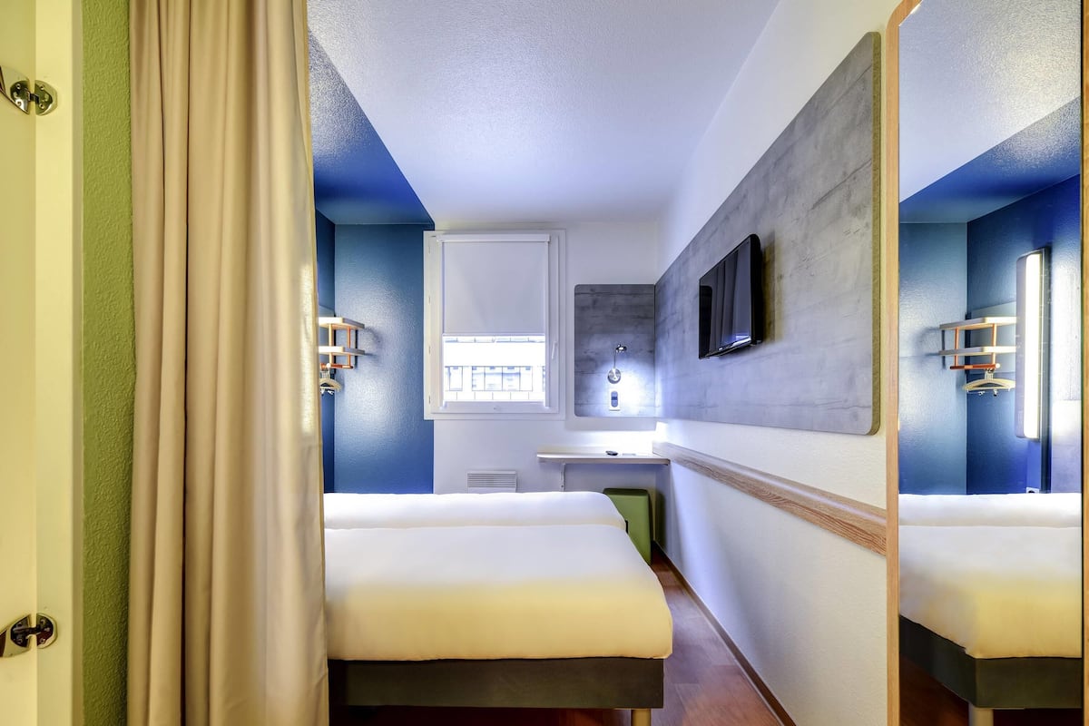 A hotel room with two beds, a bathroom, a TV, and a window.