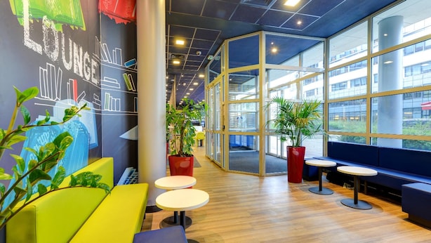 A modern lounge area with seating, tables, and large windows offering views of the building's exterior.