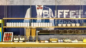 A buffet counter with a large banner, multiple serving stations, and a variety of food and drink options. - ibis budget Rueil Malmaison (Nanterre)