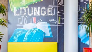 A vibrant lounge area with a yellow sofa and two white tables, a chalkboard wall with the word "LOUNGE" and abstract drawings, and a potted plant.