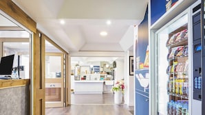 A hotel lobby with a reception desk, a vending machine, and a counter with various items. - ibis budget Santeny (Santeny)
