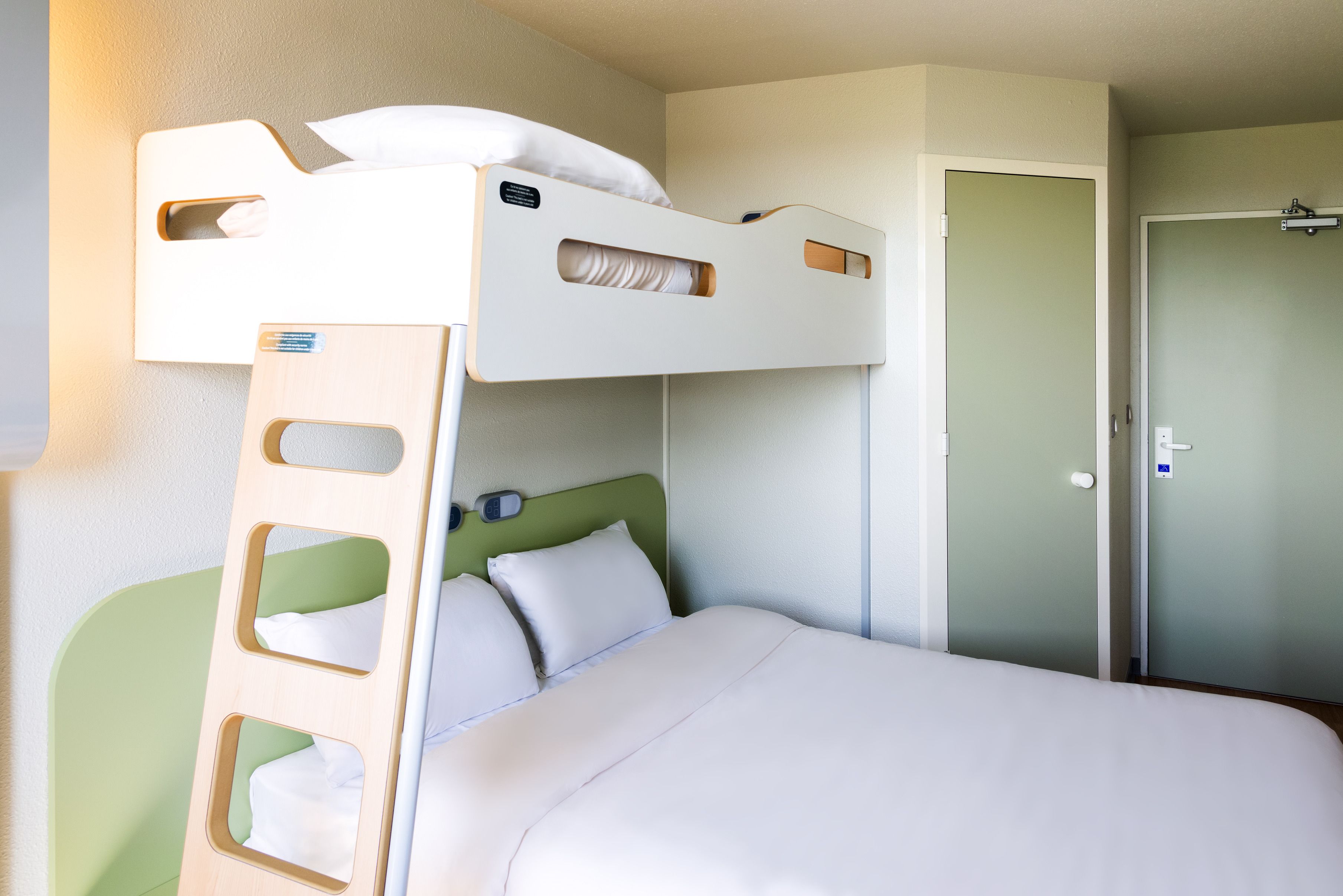Una cama litera con escalera, una mesita de noche y una puerta en una habitación de hotel.