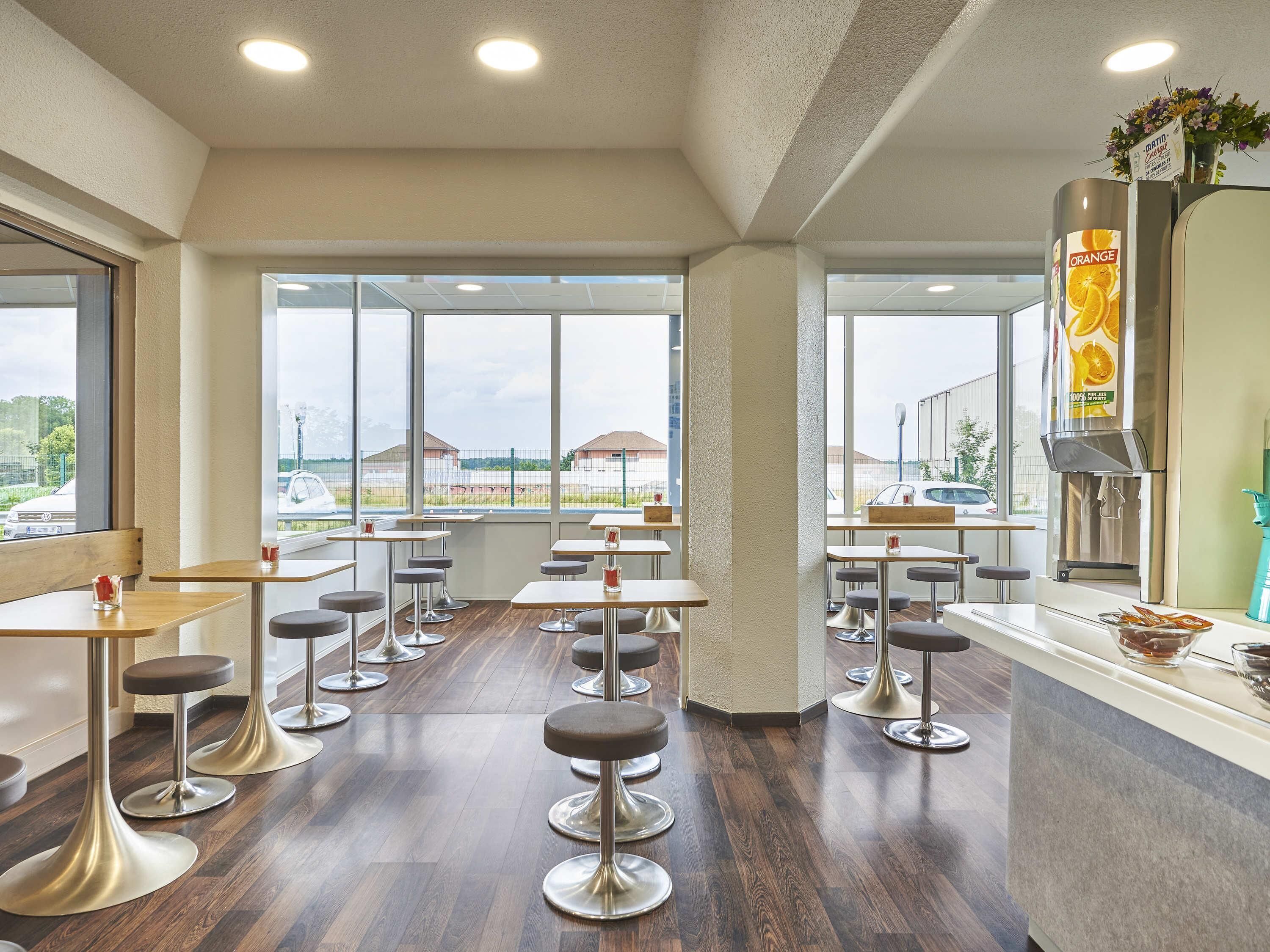 Ein modernes Restaurant mit hohen Decken, großen Fenstern und einer zentral platzierten Orangensaftmaschine.