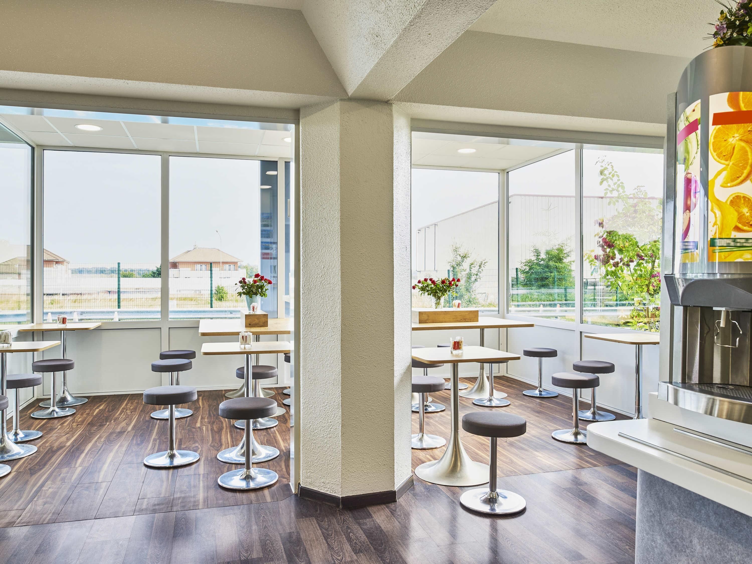 A modern bar area with multiple stools, large windows, and a bar counter.