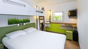 Een compacte hotelkamer met een stapelbed, een kleine kitchenette, een televisie en een raam met uitzicht.