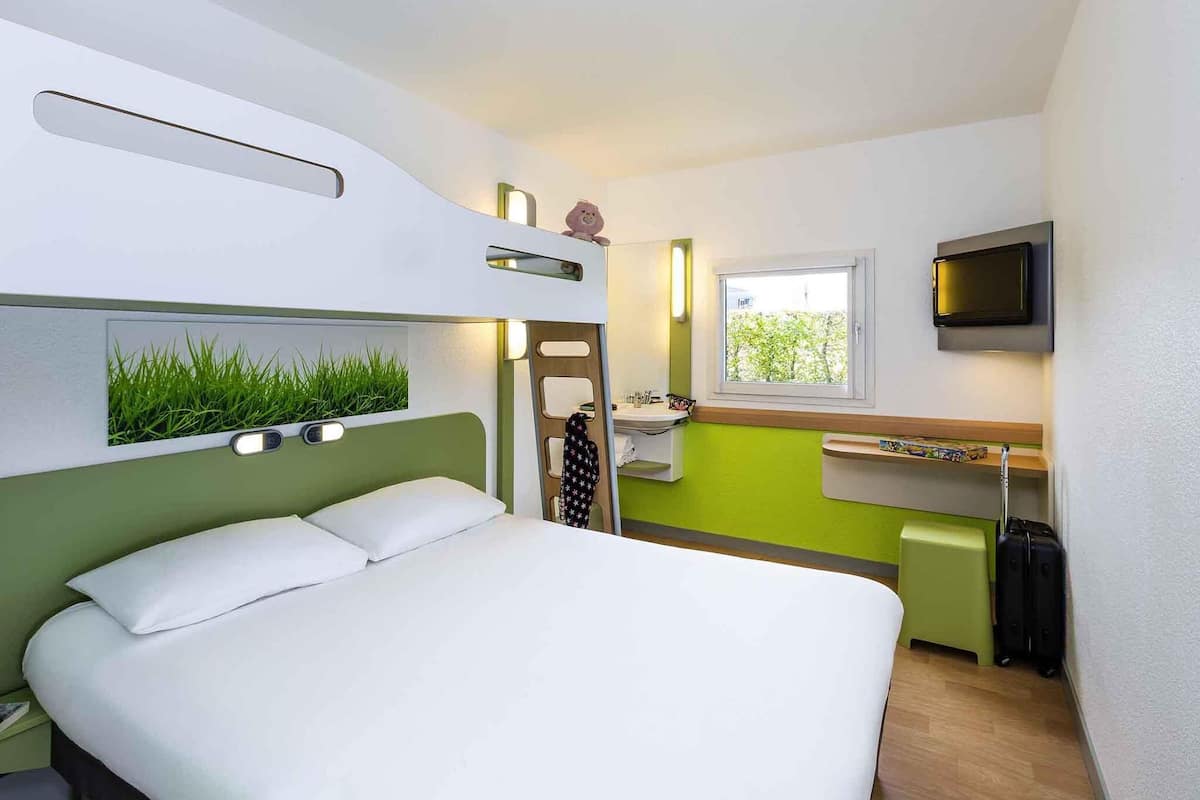 A compact hotel room with a bunk bed, a small kitchenette, a TV, and a window with a view.