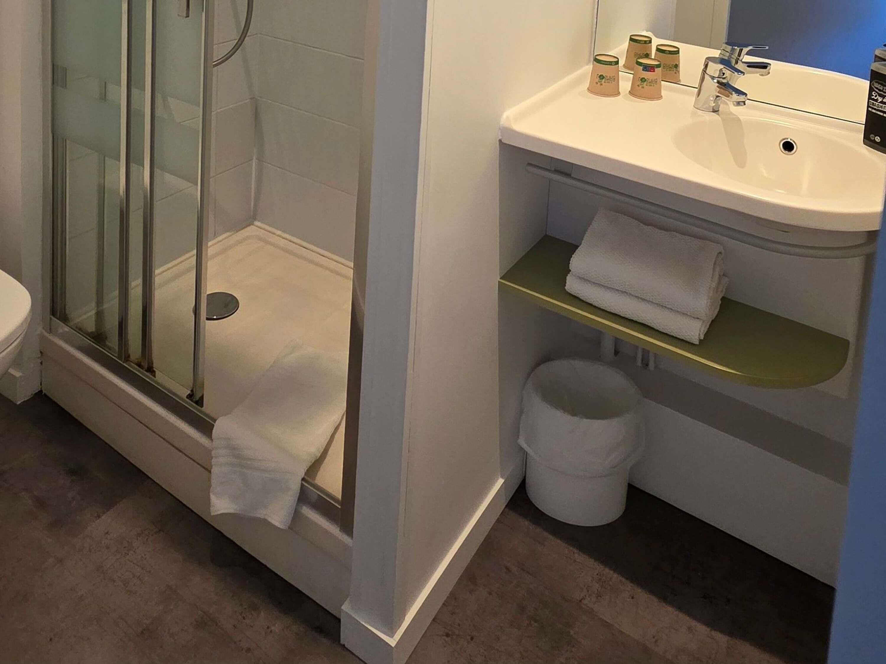 Une salle de bain avec une douche à parois de verre, un lavabo blanc avec un miroir et des toilettes.