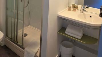 Une salle de bain avec une douche à parois de verre, un lavabo blanc avec un miroir et des toilettes.