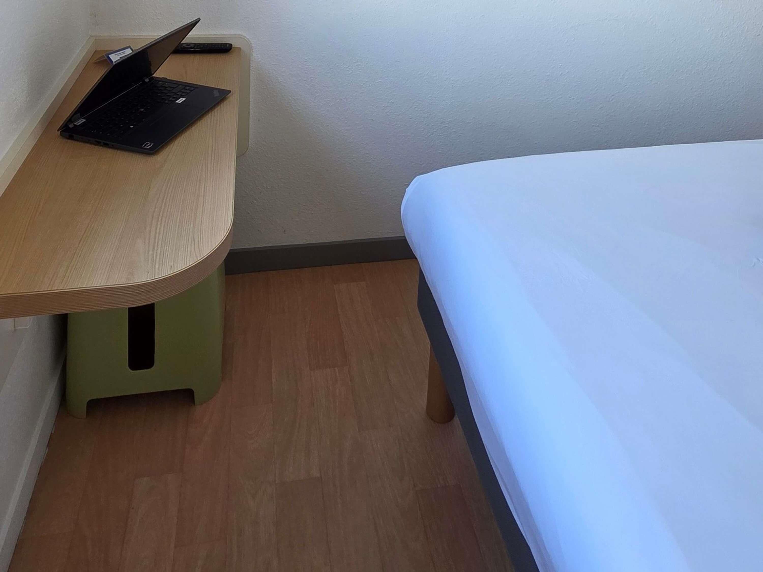 Una habitación pequeña con una cama, un escritorio con una computadora portátil y un taburete verde.