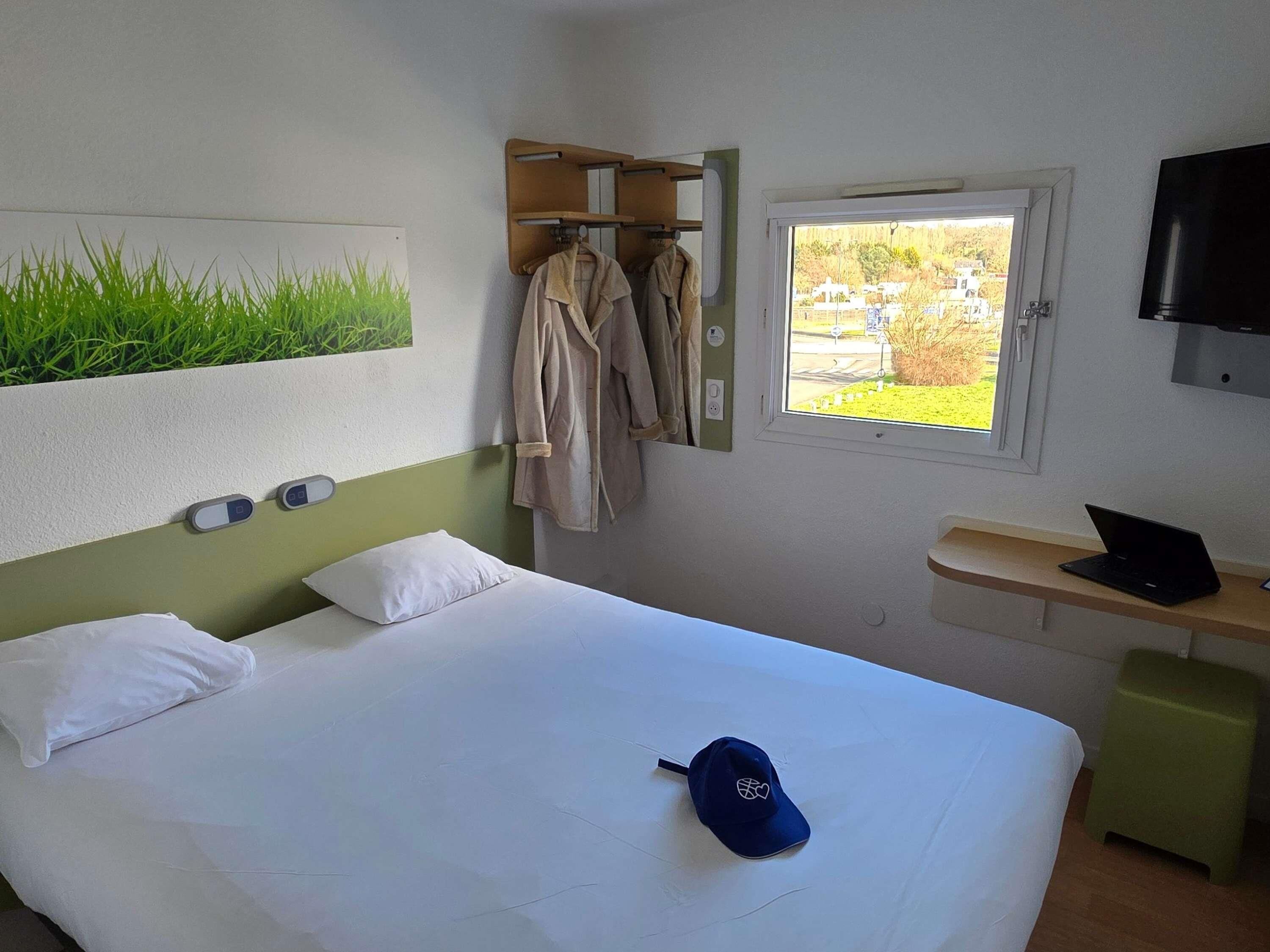 Ein Hotelzimmer mit Bett, Fenster mit Aussicht, Fernseher und Schreibtisch mit Laptop.