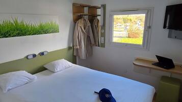 Ein Hotelzimmer mit Bett, Fenster mit Aussicht, Fernseher und Schreibtisch mit Laptop.