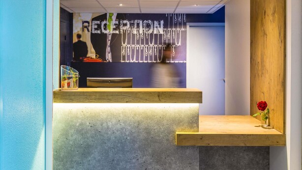 Een modern ontworpen receptiebalie, met een betonnen aanrecht en een houten paneel aan de rechterkant.