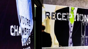 Un área de recepción con un letrero que dice "RECEPTION" y otro letrero con texto parcialmente visible que parece decir "YOUR CHAMBRE" y "ATTEND".