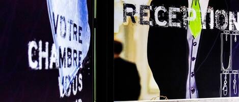 Un espace d’accueil avec une enseigne indiquant « RÉCEPTION » et une autre enseigne dont le texte est partiellement visible et qui semble indiquer « VOTRE CHAMBRE » et « ATTENDEZ ».