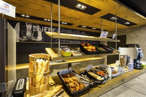 Zona de bufé con diferentes opciones de comida, como pan, frutas y bebidas.