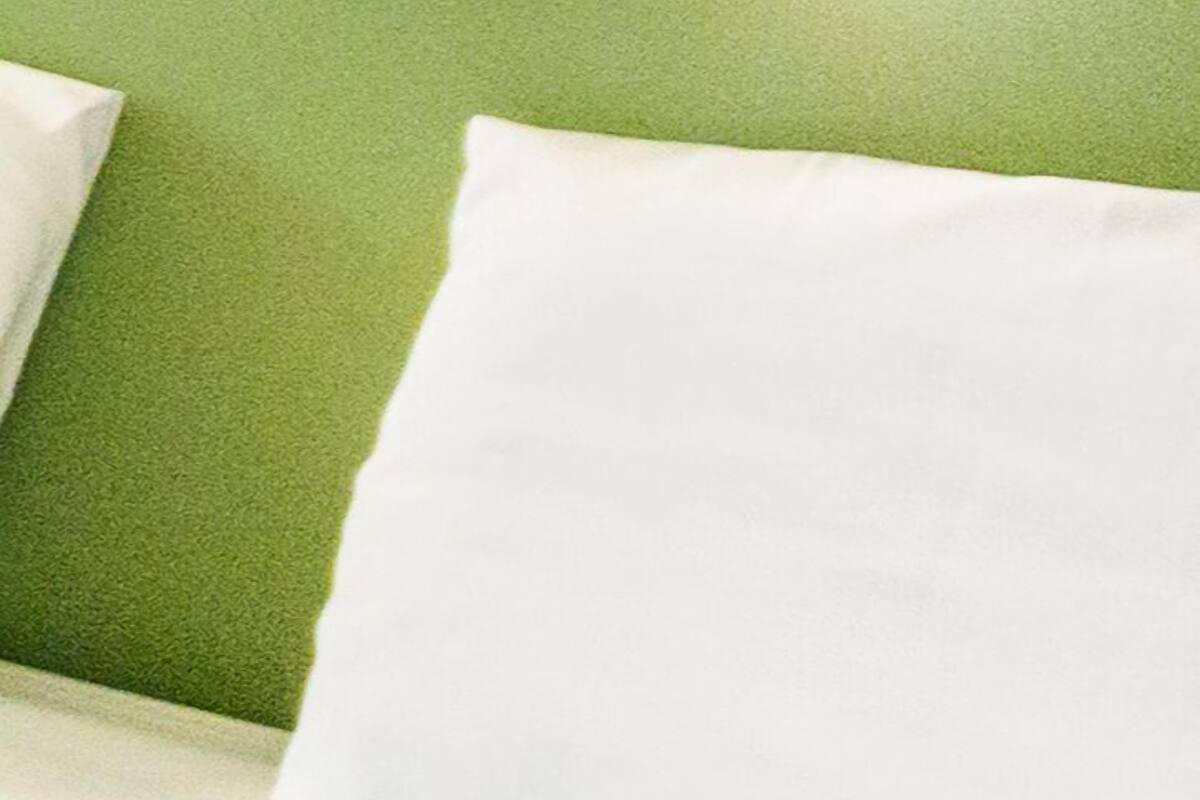 Uma cama com roupa de cama branca e uma parede verde ao fundo.