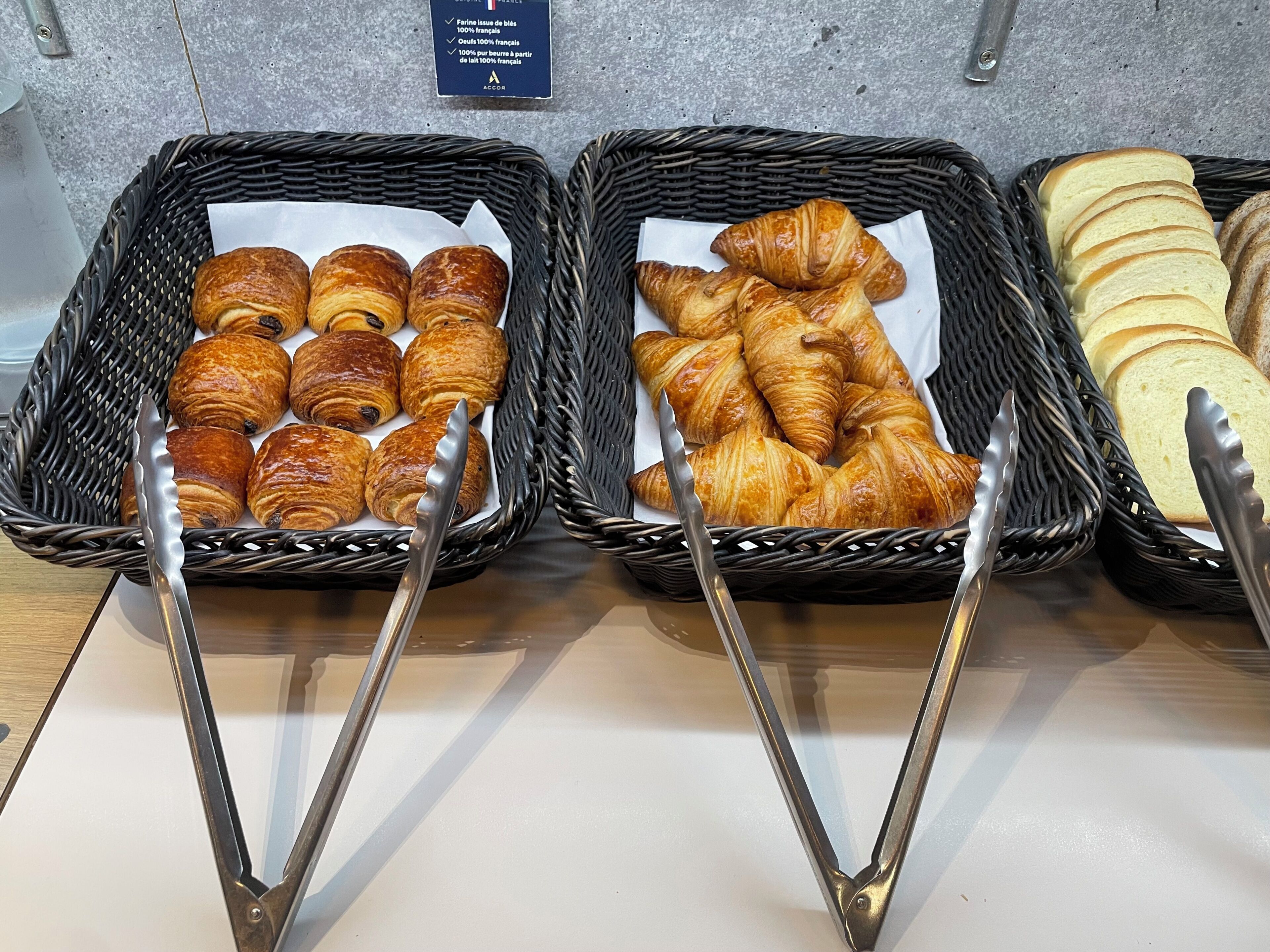Three baskets of baked goods with tongs, placed on a counter.