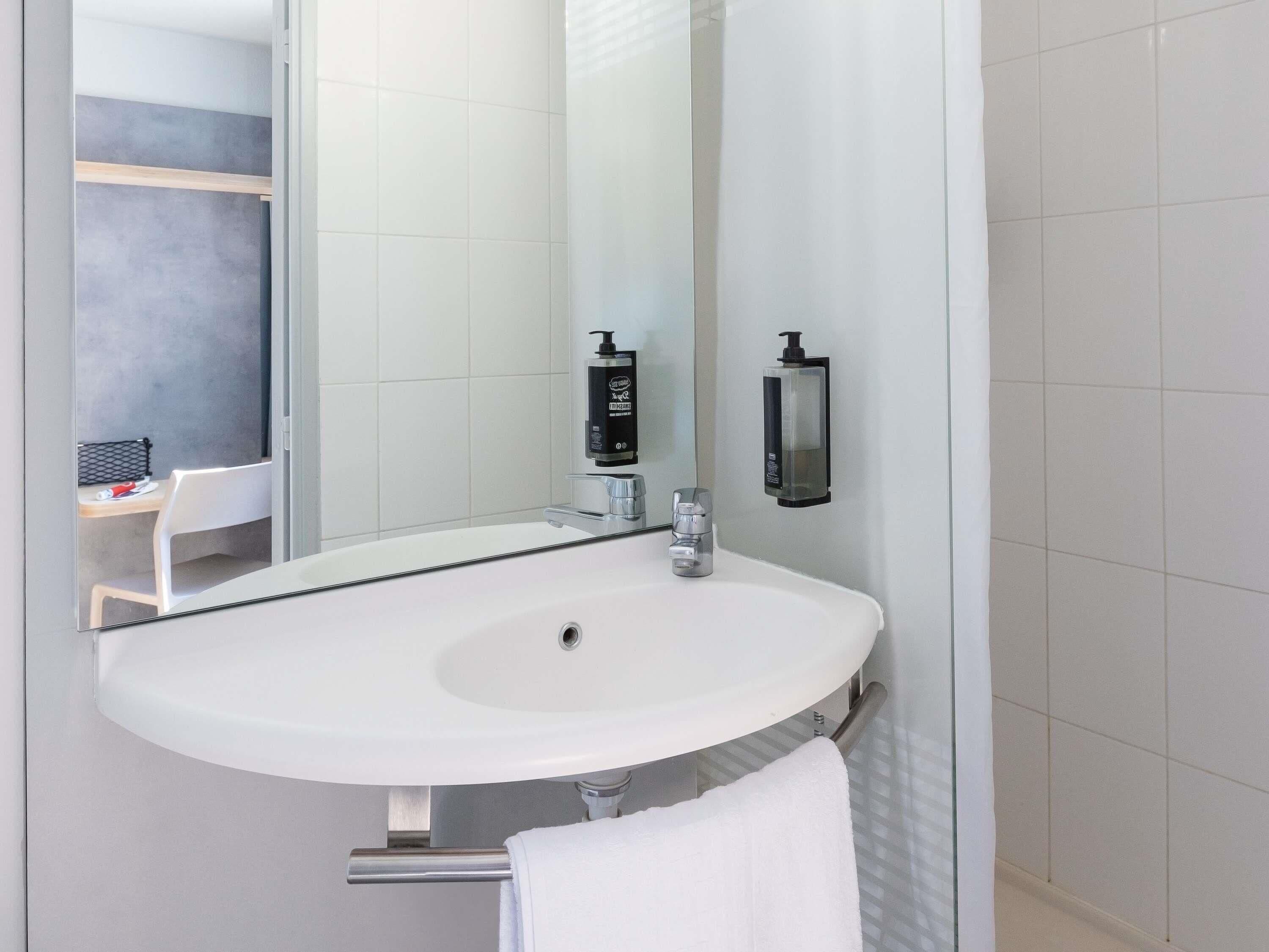 Un baño moderno con un lavamanos blanco, un espejo y un perchero para toallas.