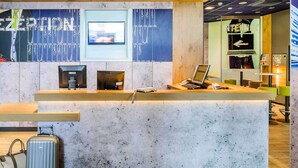 A reception desk with a computer, a television, and a coffee machine. - ibis budget Deauville (Saint-Arnoult)