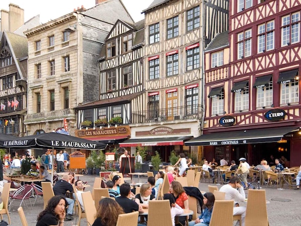 A European street with outdoor seating at cafes, historic buildings, and signs for 'LE MAUPASSANT' and 'L'EURO' restaurants.