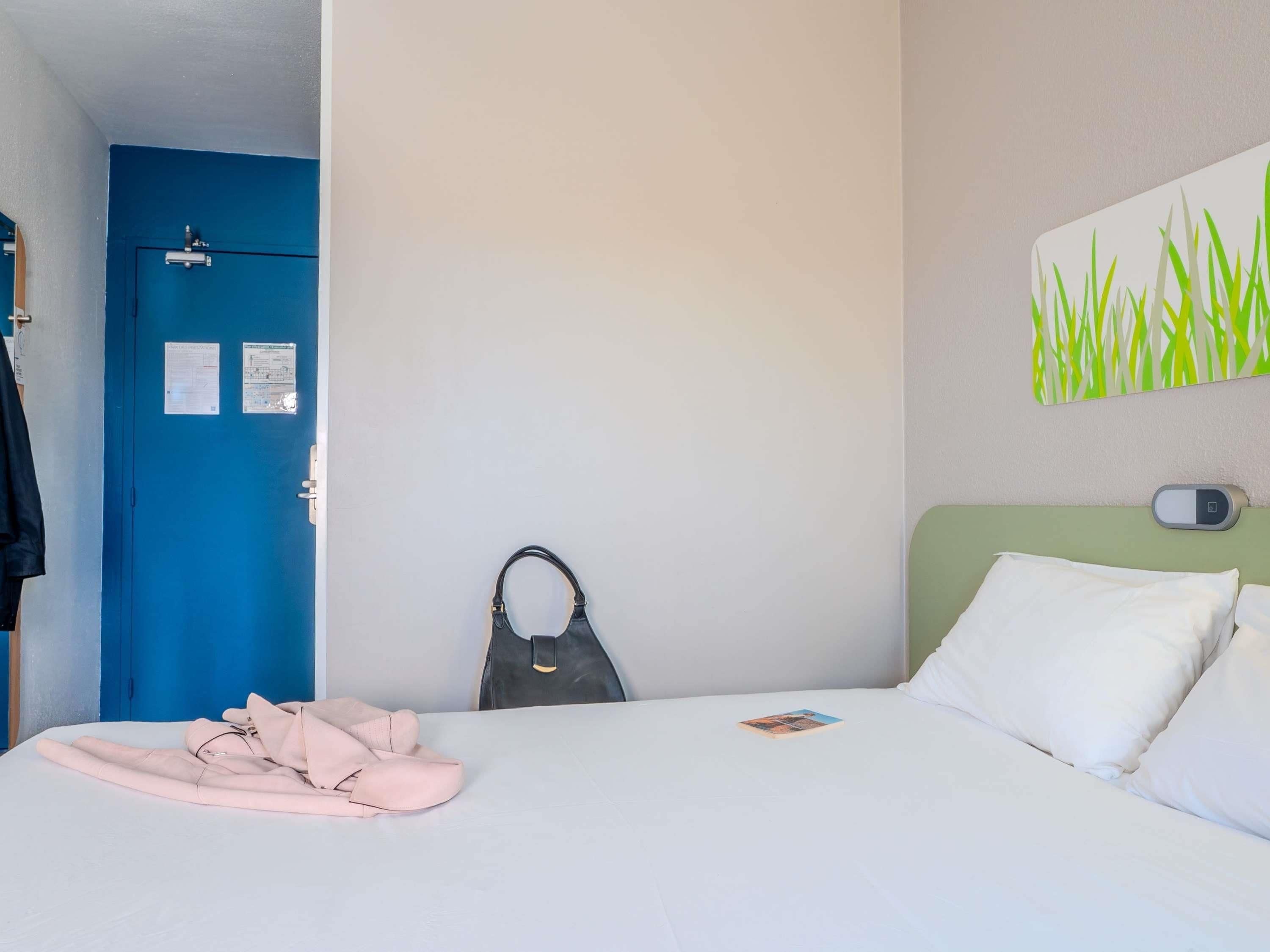 Habitación de hotel con cama, una puerta azul, un termostato fijado a la pared y un cuadro de hierba.