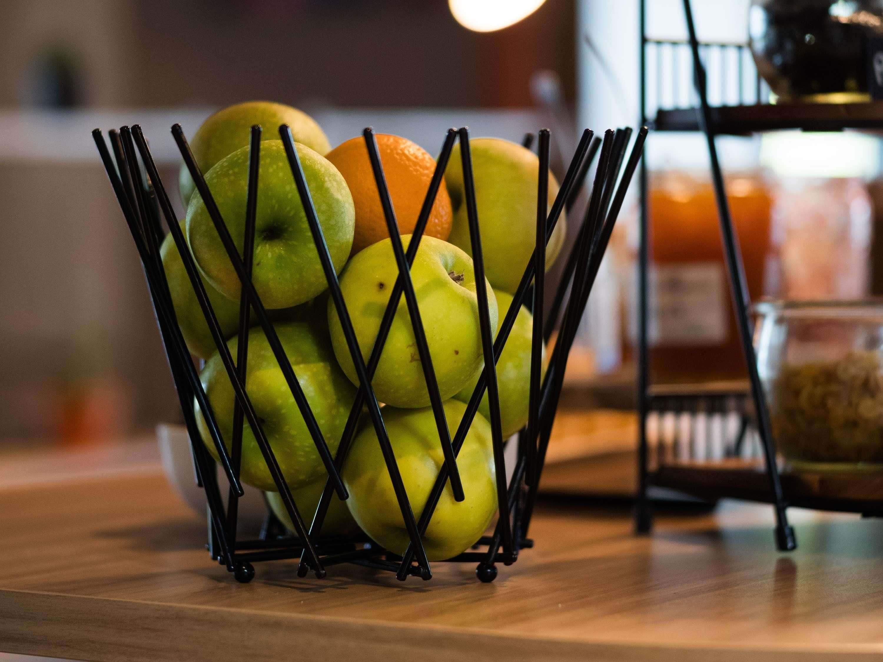 Uma cesta de frutas com maçãs e laranjas sobre uma superfície de madeira.