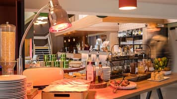 Een buffetopstelling met diverse gerechten, een drankstation en een bar op de achtergrond.