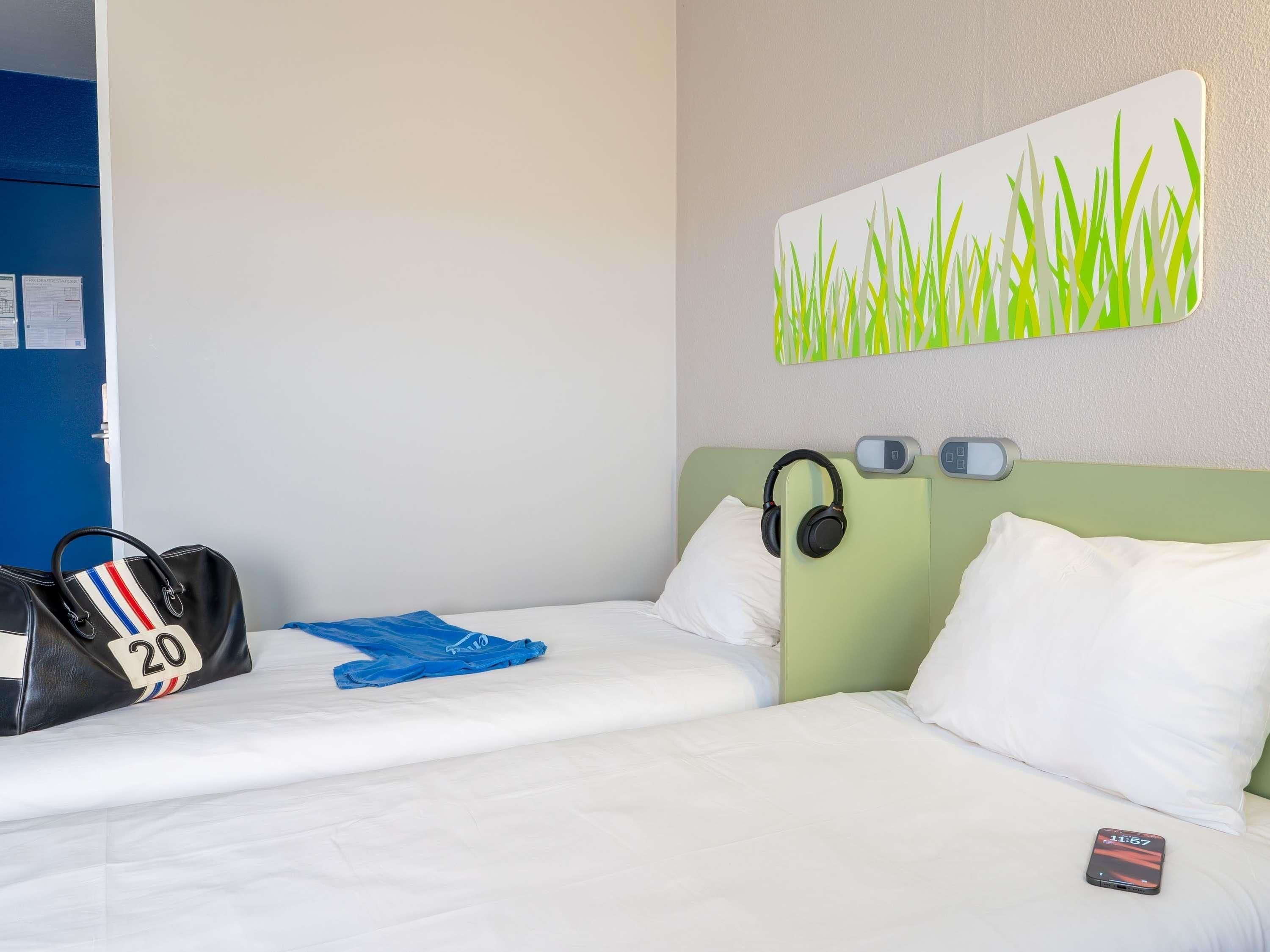 Quarto de hotel com cama, fones de ouvido, smartphone e bolsa com um número.
