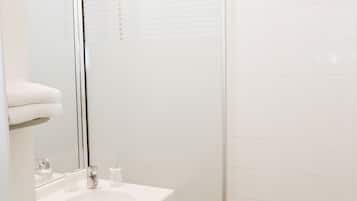 Un baño moderno con cabina de ducha de vidrio, un lavabo blanco y un inodoro.