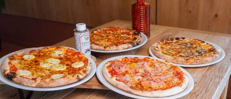 Four pizzas on a wooden table with a pizza cutter and a can of beer.