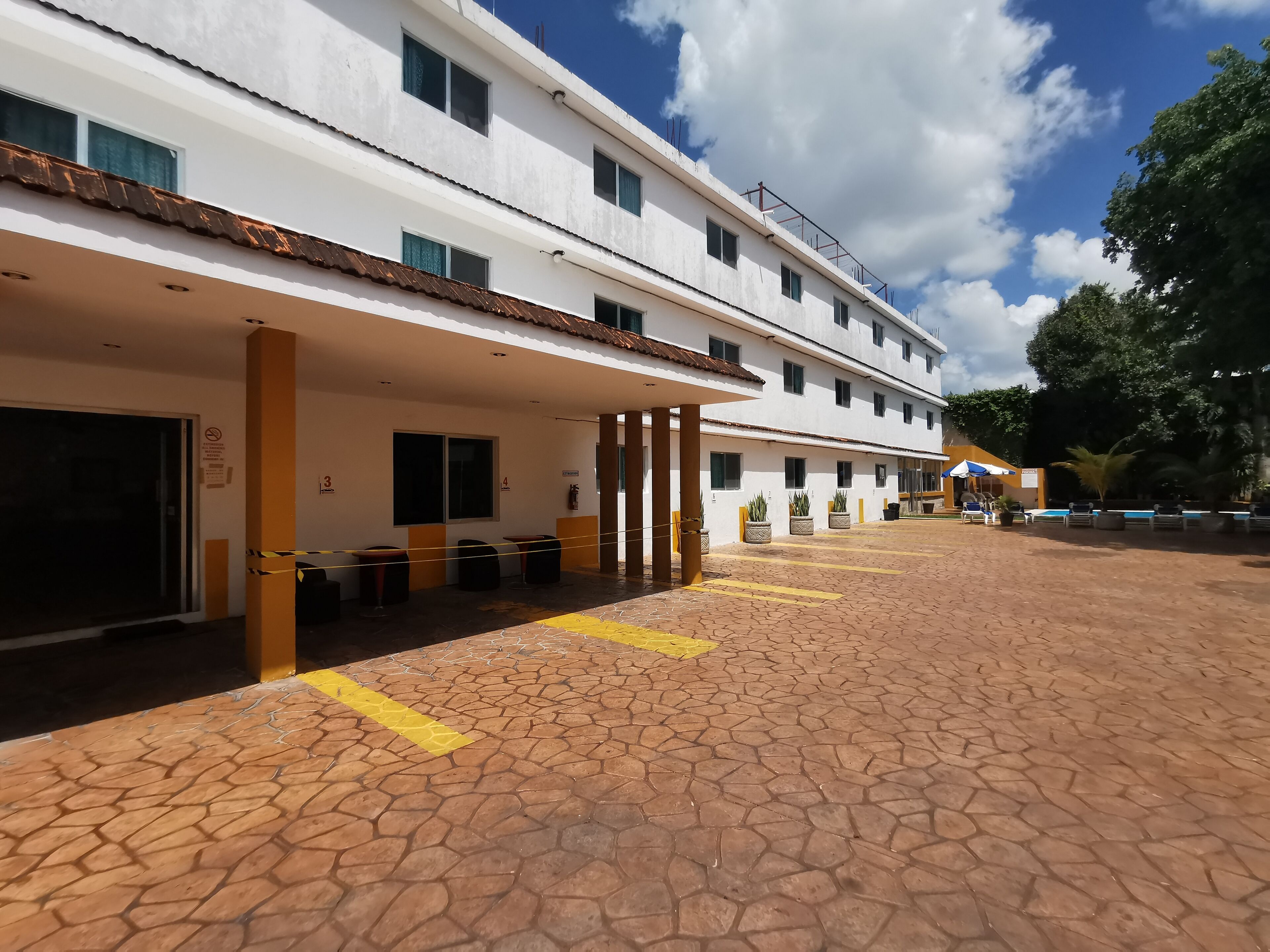 Un edificio de varios pisos con un área de acceso cubierta, asientos al aire libre y una piscina.