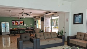 A spacious lobby with a sofa, chairs, a coffee table, ceiling fans, a refrigerator, and a dining area with a table and chairs. - Las Dalias Inn (Mérida)